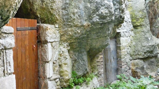 Eine rustikale Steinwand mit einer Holztür, auf der “C. Goin” steht.