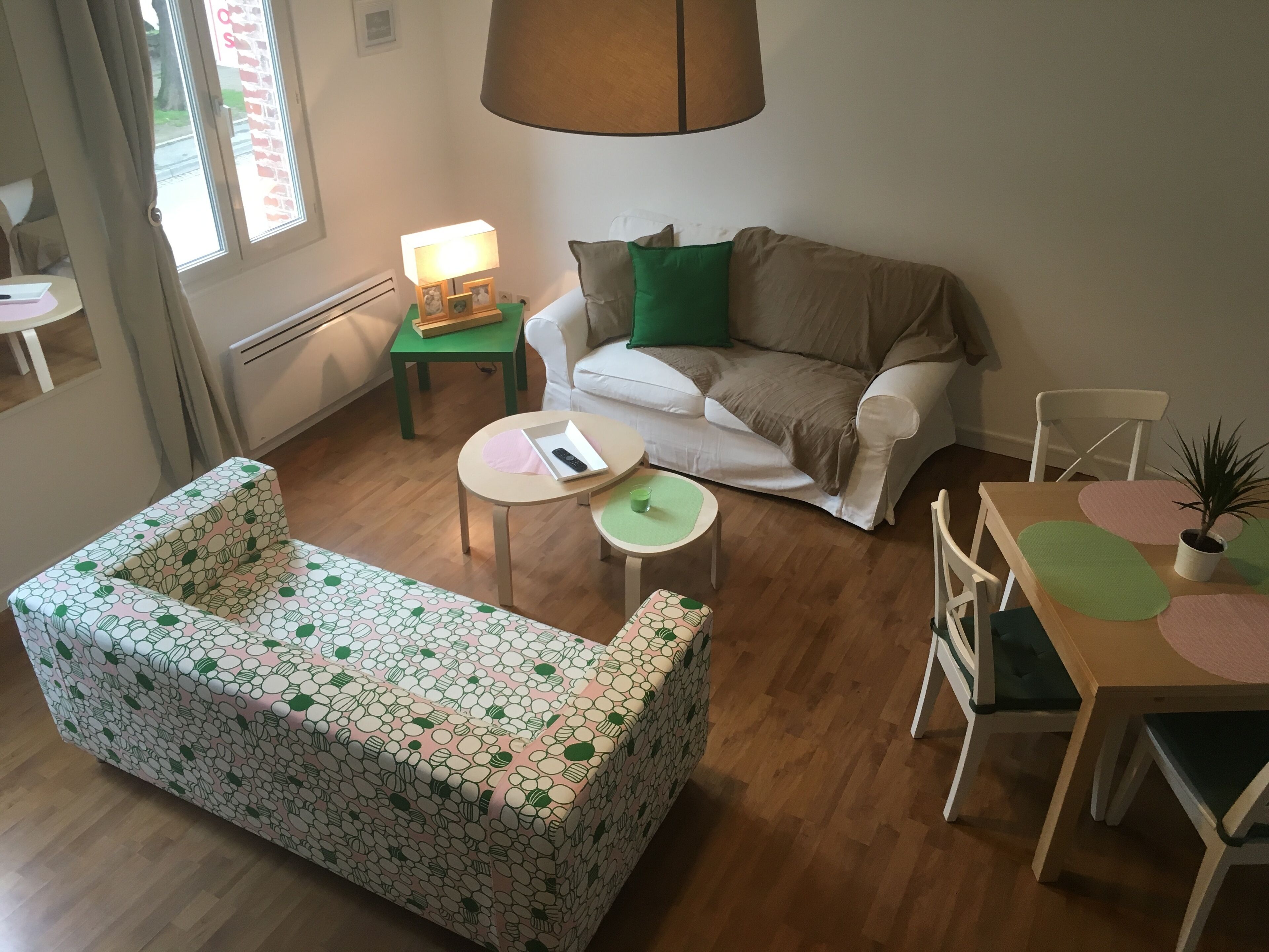 Een gezellige zithoek met een gestreept sofa, een klein rond tafeltje, een groen bijzettafeltje, een witte bank en een eettafel met stoelen.