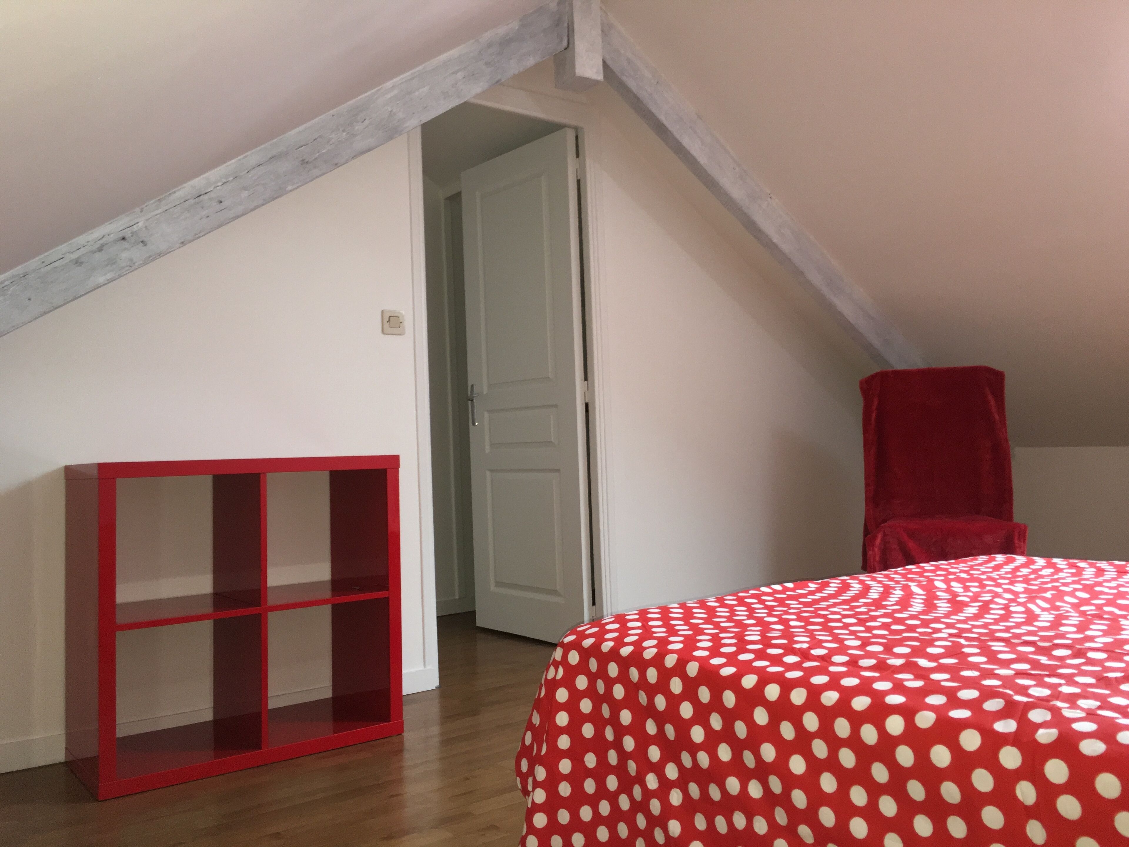 Une chambre avec une couvre-lit à pois rouges, une chaise rouge et une étagère rouge.