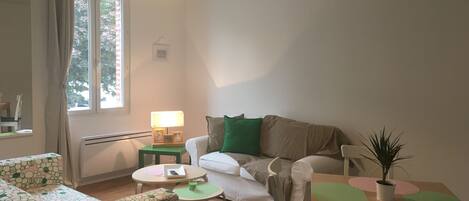 A cozy living room with a sofa, a small table, a lamp, and a potted plant.
