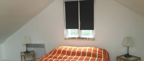 A bedroom with a bed, two nightstands, a window with blinds, and a radiator.