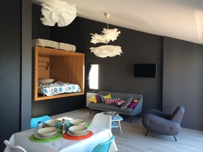 Una sala moderna con un sofá, una mesa de comedor con platos y vasos, un estante de madera con una cama y un televisor montado.