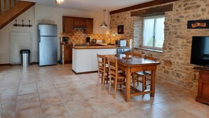 Una cocina con una isla central, una mesa de comedor de madera y sillas. Hay un refrigerador, estufa y microondas. La cocina tiene paredes de piedra y una ventana.