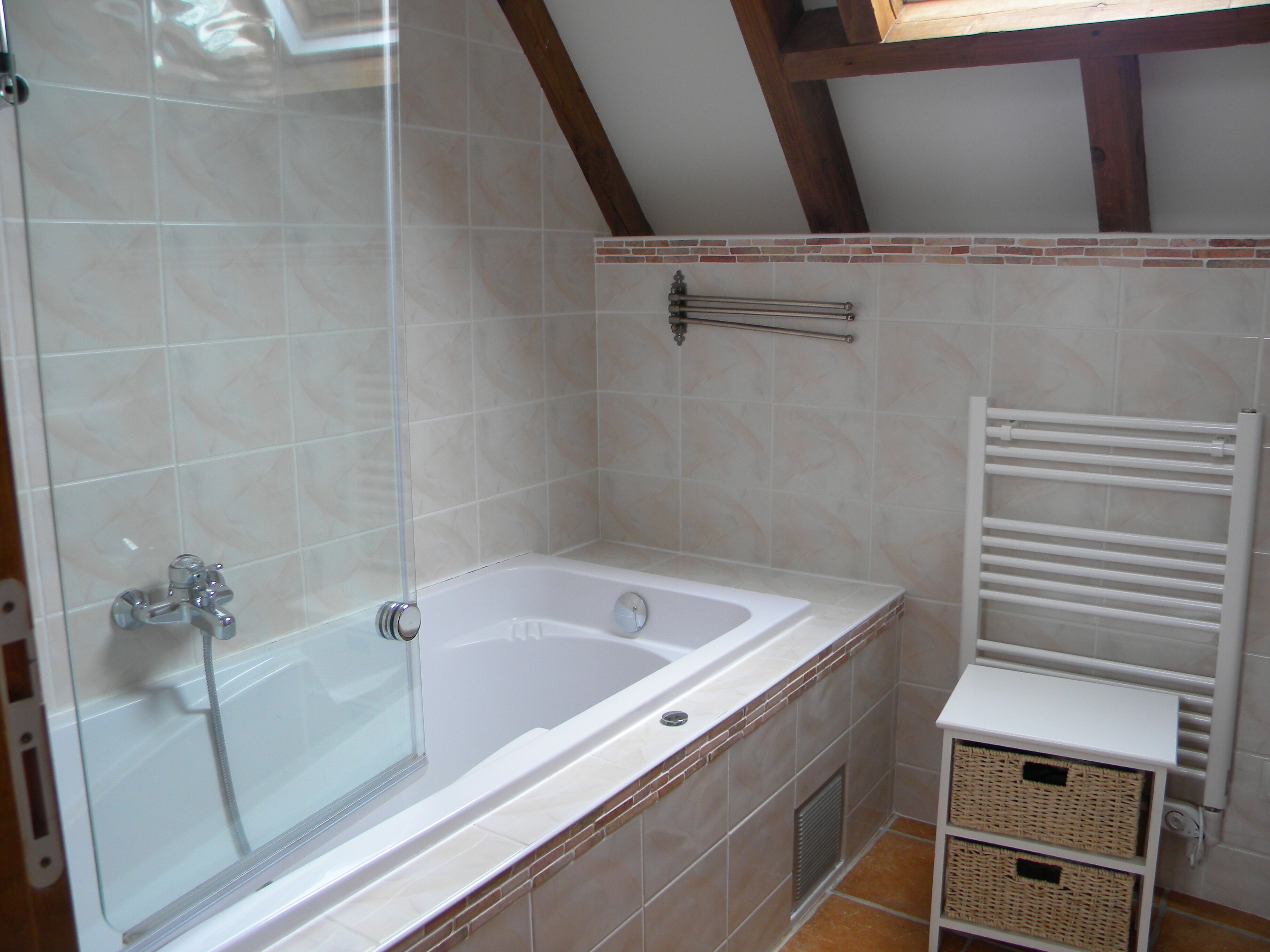 A bathroom with a bathtub, a glass shower enclosure, a towel rack, and wicker baskets on a shelf.