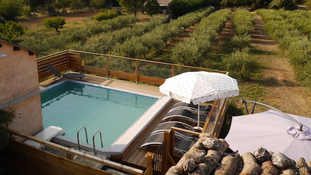 Un área de piscina con cubierta de madera, sillas de descanso y una sombrilla.