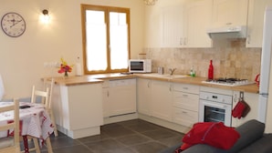 Cocina compacta con microondas, estufa y armarios. Cuenta con una mesa de comedor con sillas y un sofá en la zona de estar.