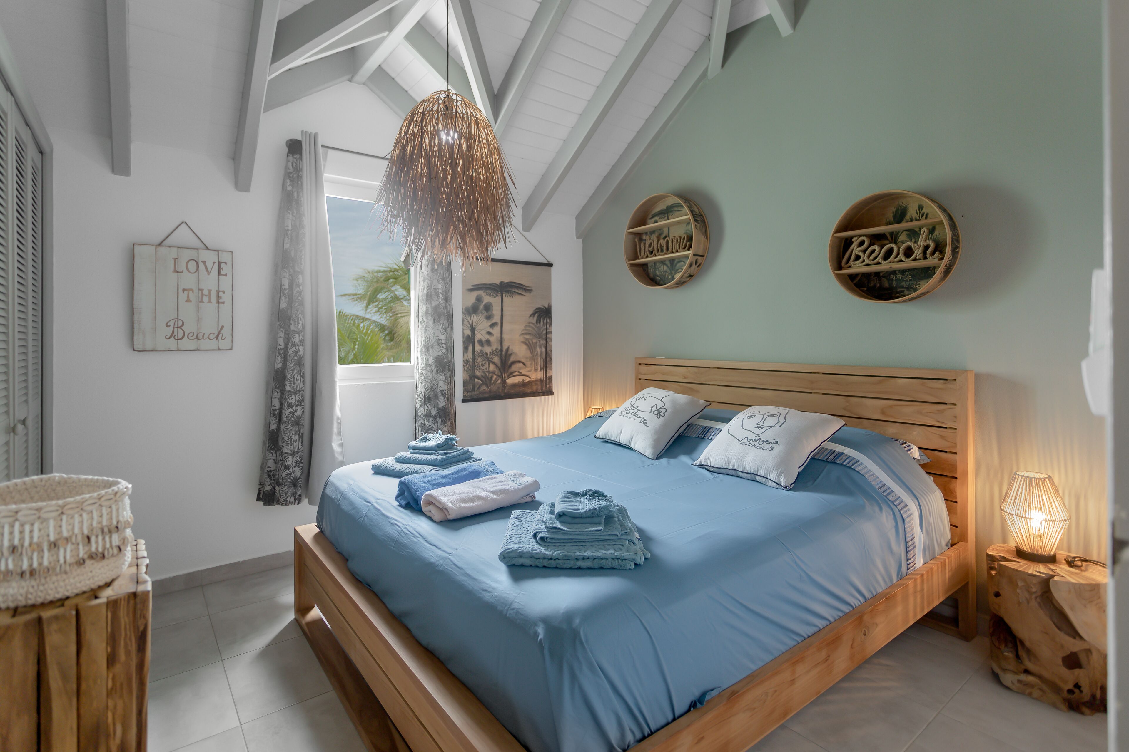 Un dormitorio con cama de madera, ropa de cama azul, lámpara colgante y adornos en la pared.