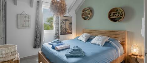 Un dormitorio con cama de madera, ropa de cama azul, lámpara colgante y adornos en la pared.