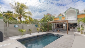 Una piscina con muelle de madera, un patio cubierto y una casa con balcón.