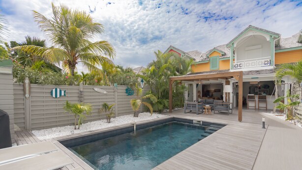 Une piscine avec une terrasse en bois, un patio couvert et une maison dotée d’un balcon.