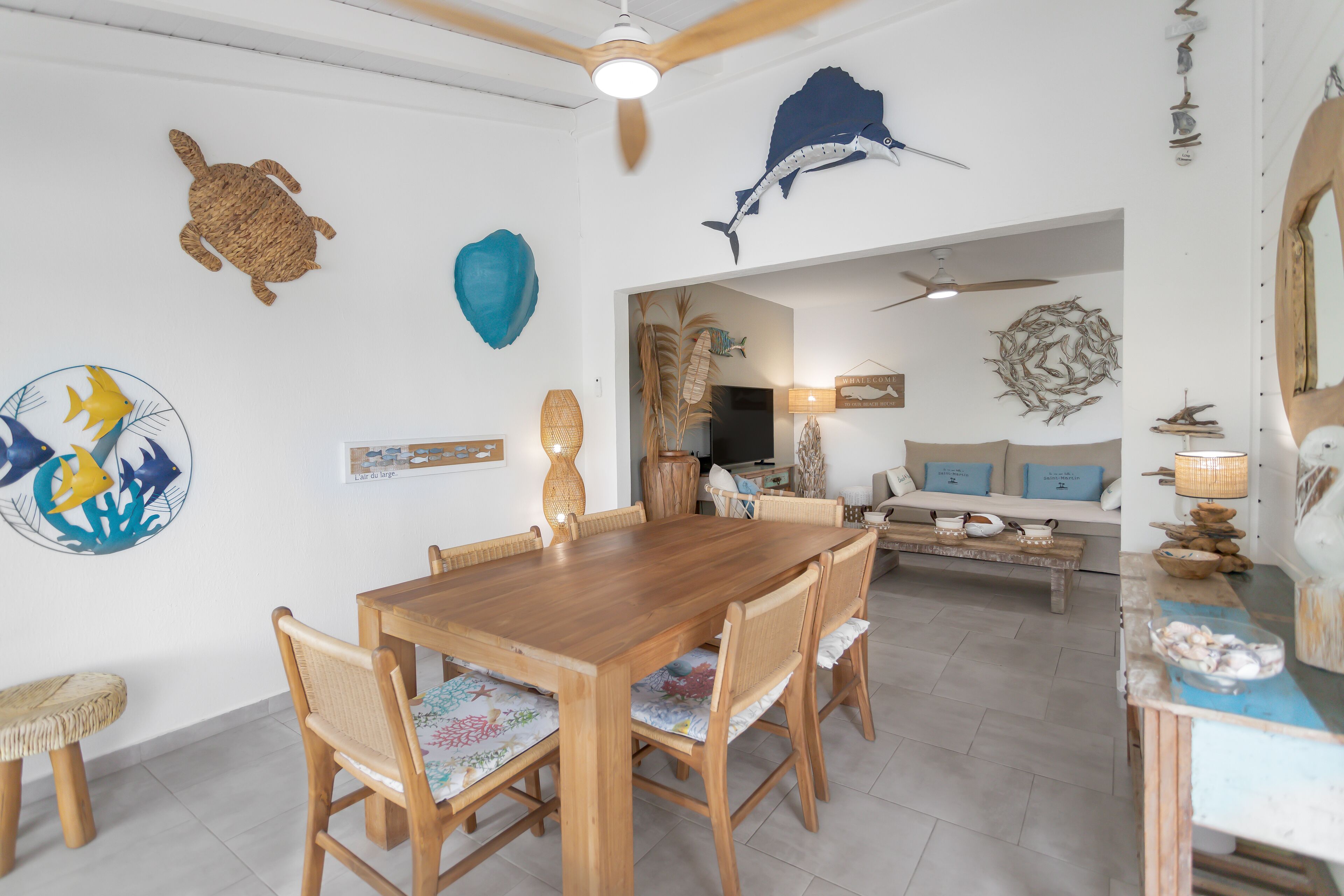 Een zithoek met een houten tafel en stoelen, een bank en decoratieve wandkunst, waaronder een schildpad en een haai.