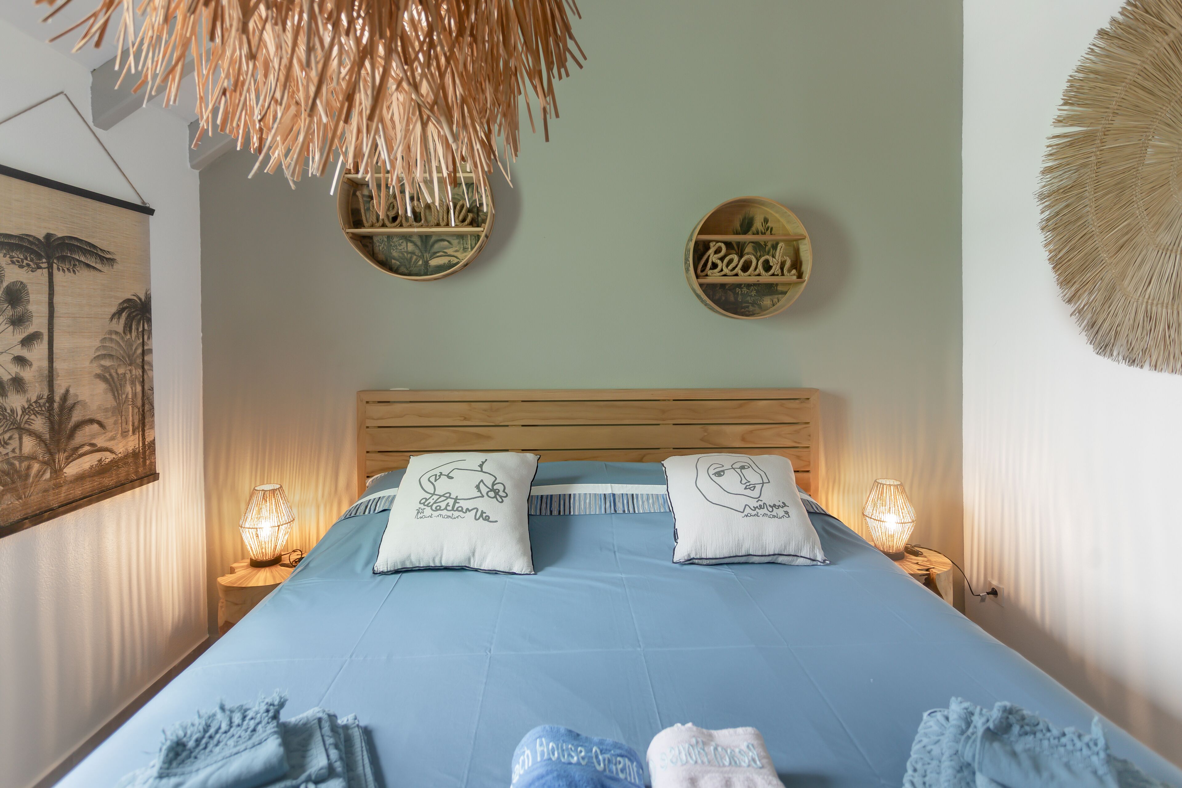 A neatly made bed with two pillows, a wall-mounted mirror, and a wall art piece.