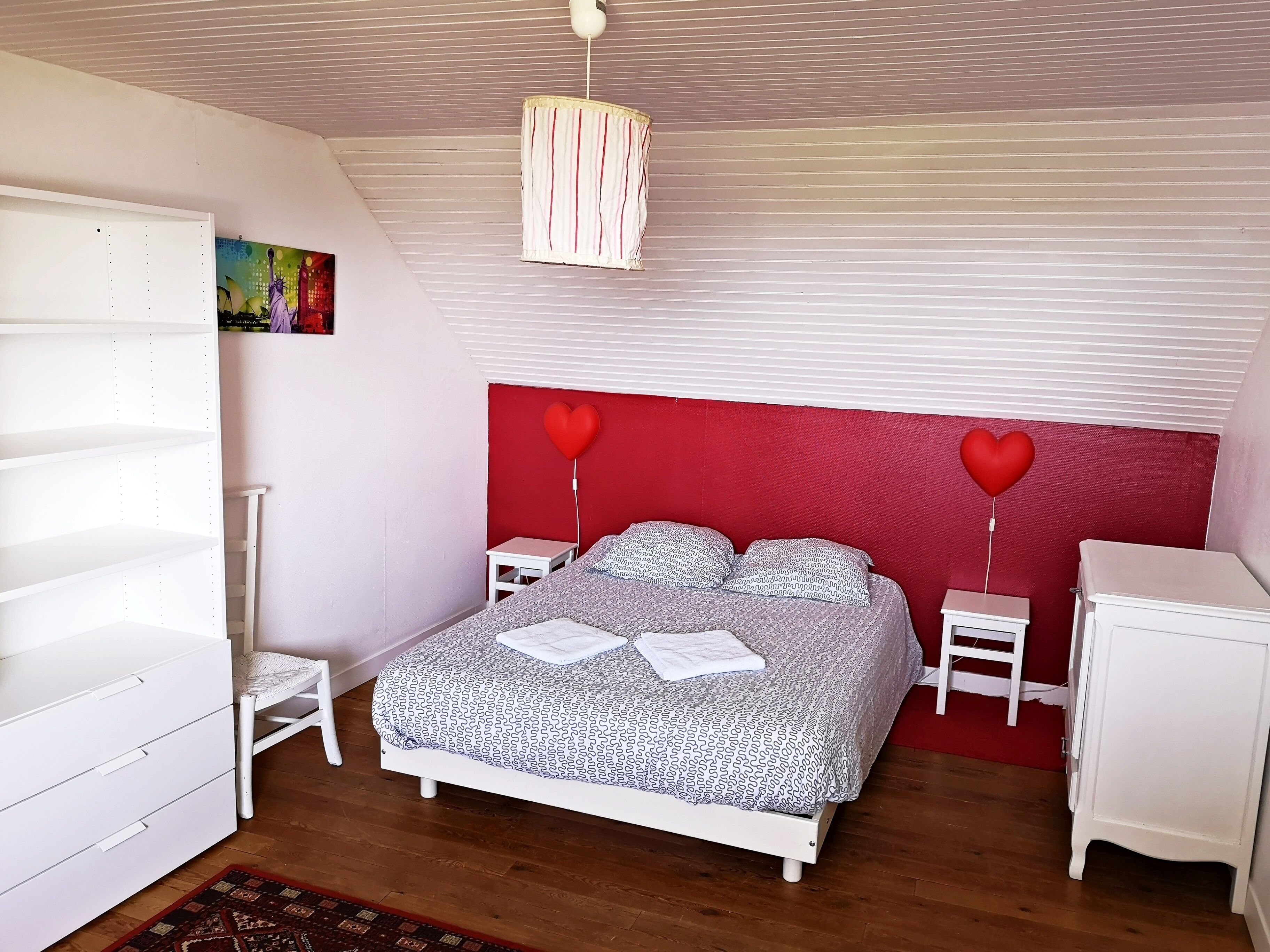 Une chambre à coucher avec un lit, une armoire blanche, des tables de chevet et un luminaire suspendu.