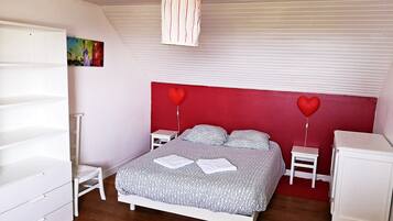 Une chambre à coucher avec un lit, une armoire blanche, des tables de chevet et un luminaire suspendu.