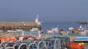 Un port où des bateaux sont amarrés, un phare et des filets de pêche sur la plage.