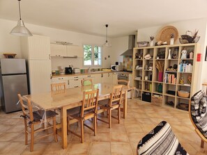 A kitchen with a dining table, chairs, a refrigerator, a microwave, and a bookshelf filled with books and decorative items.
