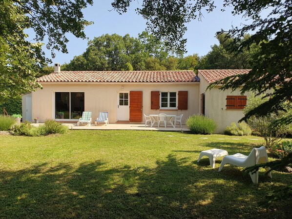 A house with a tiled roof, a patio with chairs, and a lawn.
