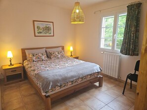 A bedroom with a bed, two bedside lamps, a window with curtains, a radiator, and a picture on the wall.