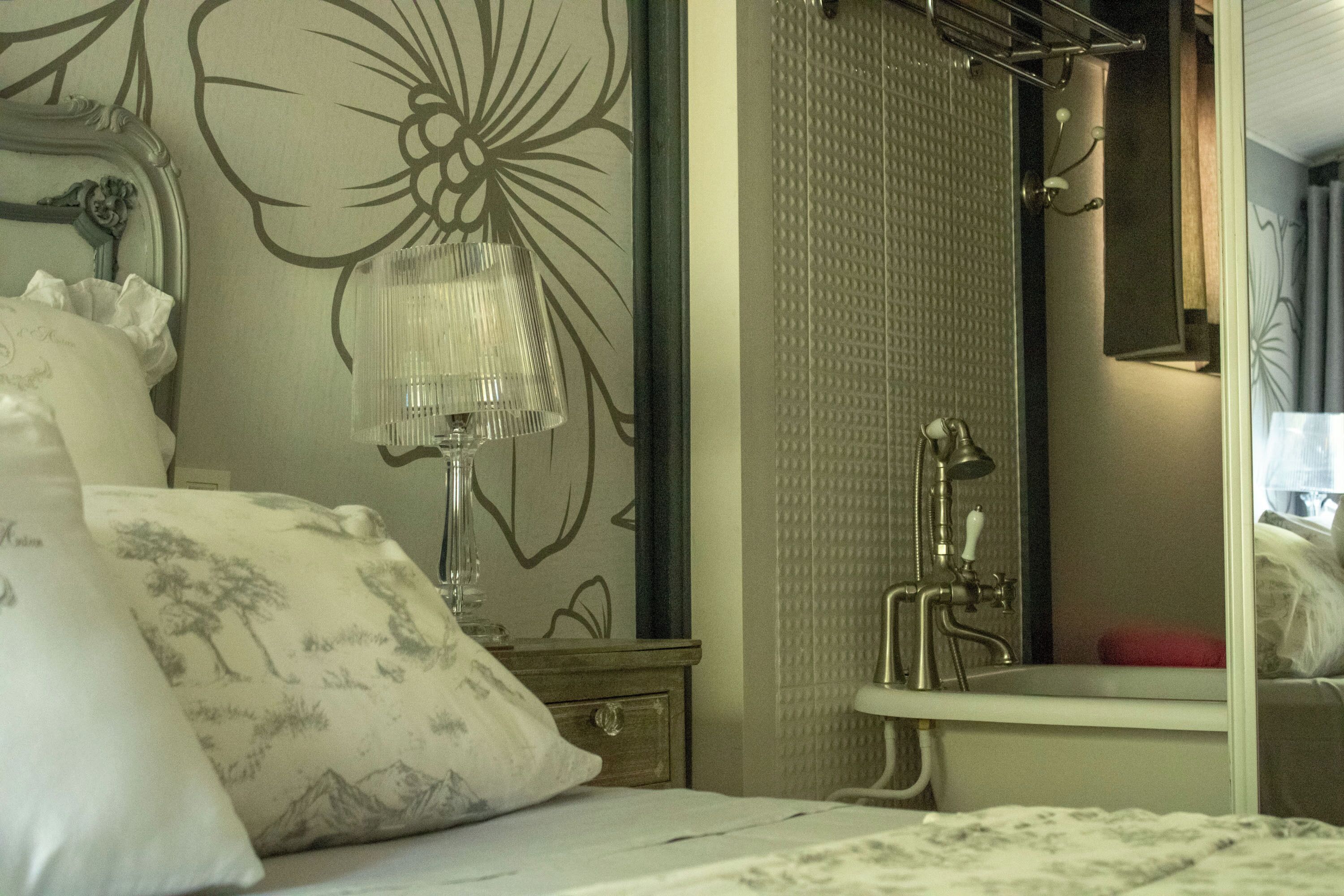 A bedroom with a bed, a nightstand, a mirror, and a bathroom with a sink and shower.