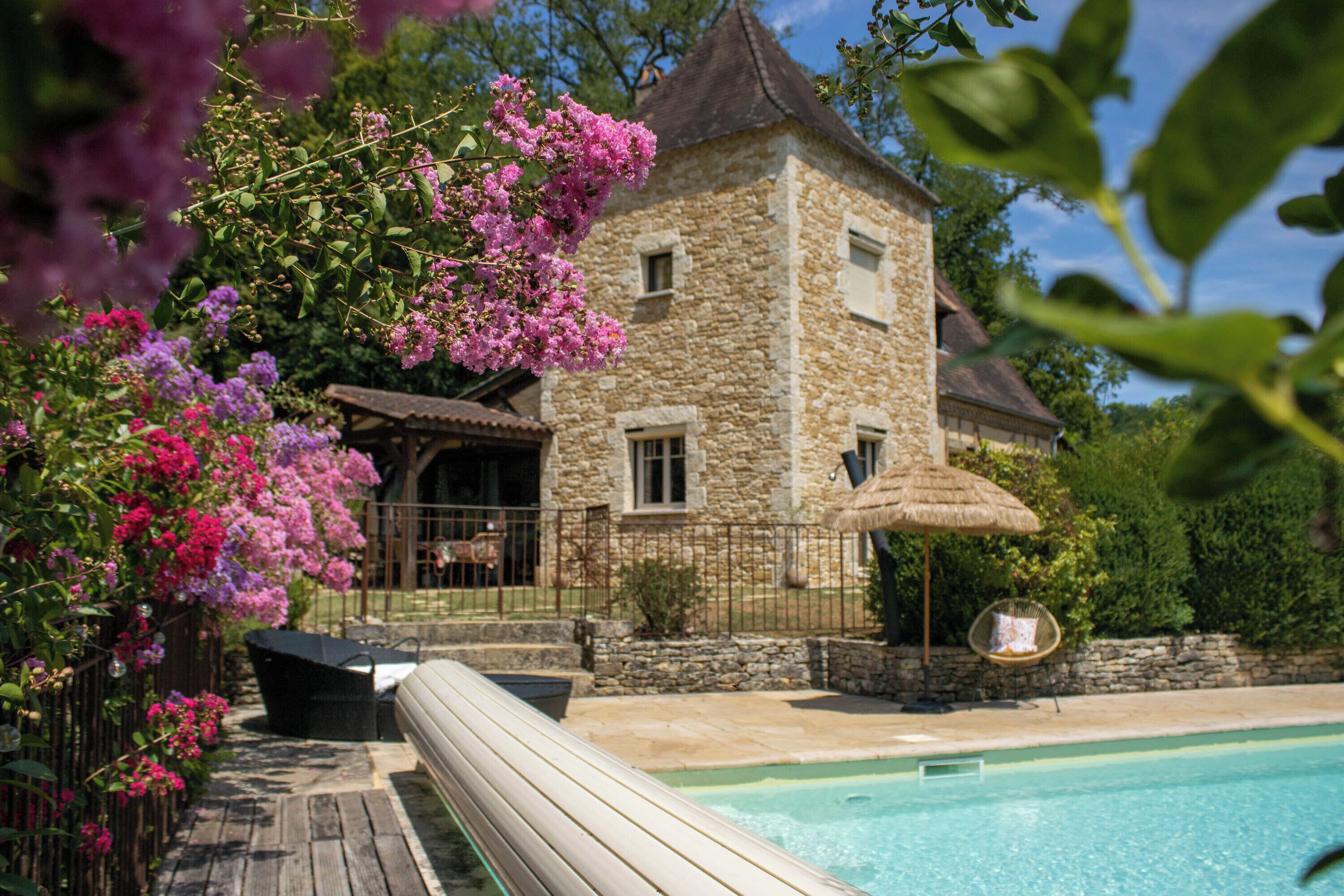 A stone building with a pool, surrounded by lush greenery and flowering plants.