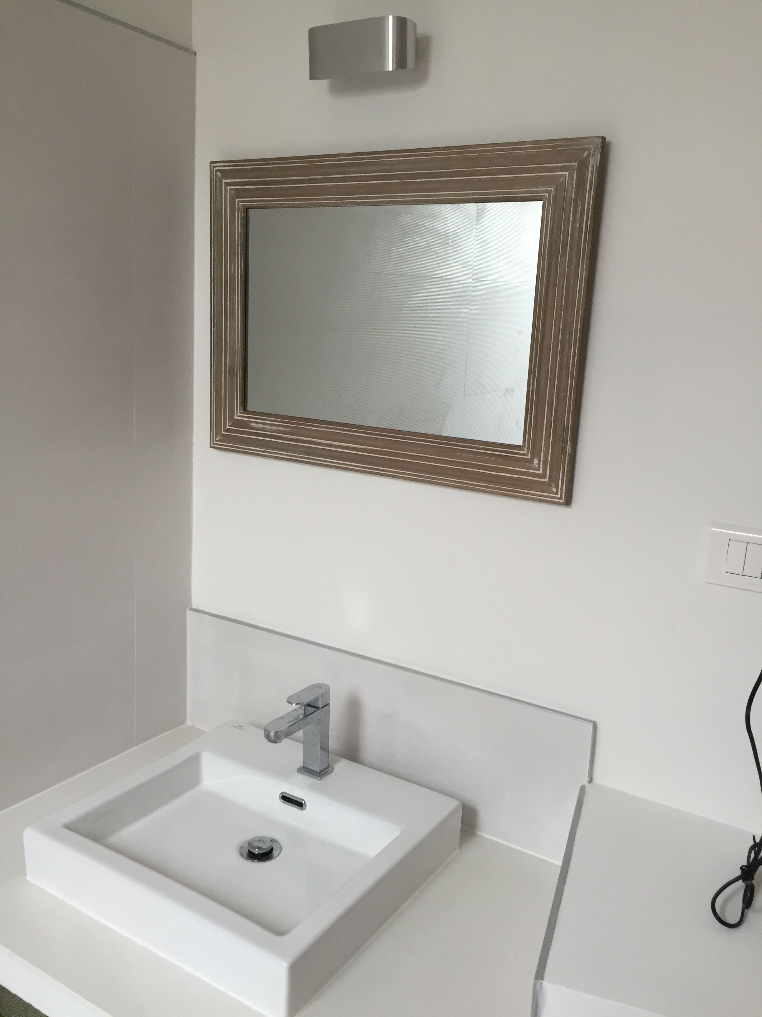 A bathroom with a white sink, a mirror with a wooden frame, and a light switch on the wall.