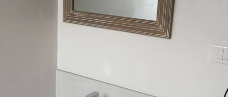 A bathroom with a white sink, a mirror with a wooden frame, and a light switch on the wall.