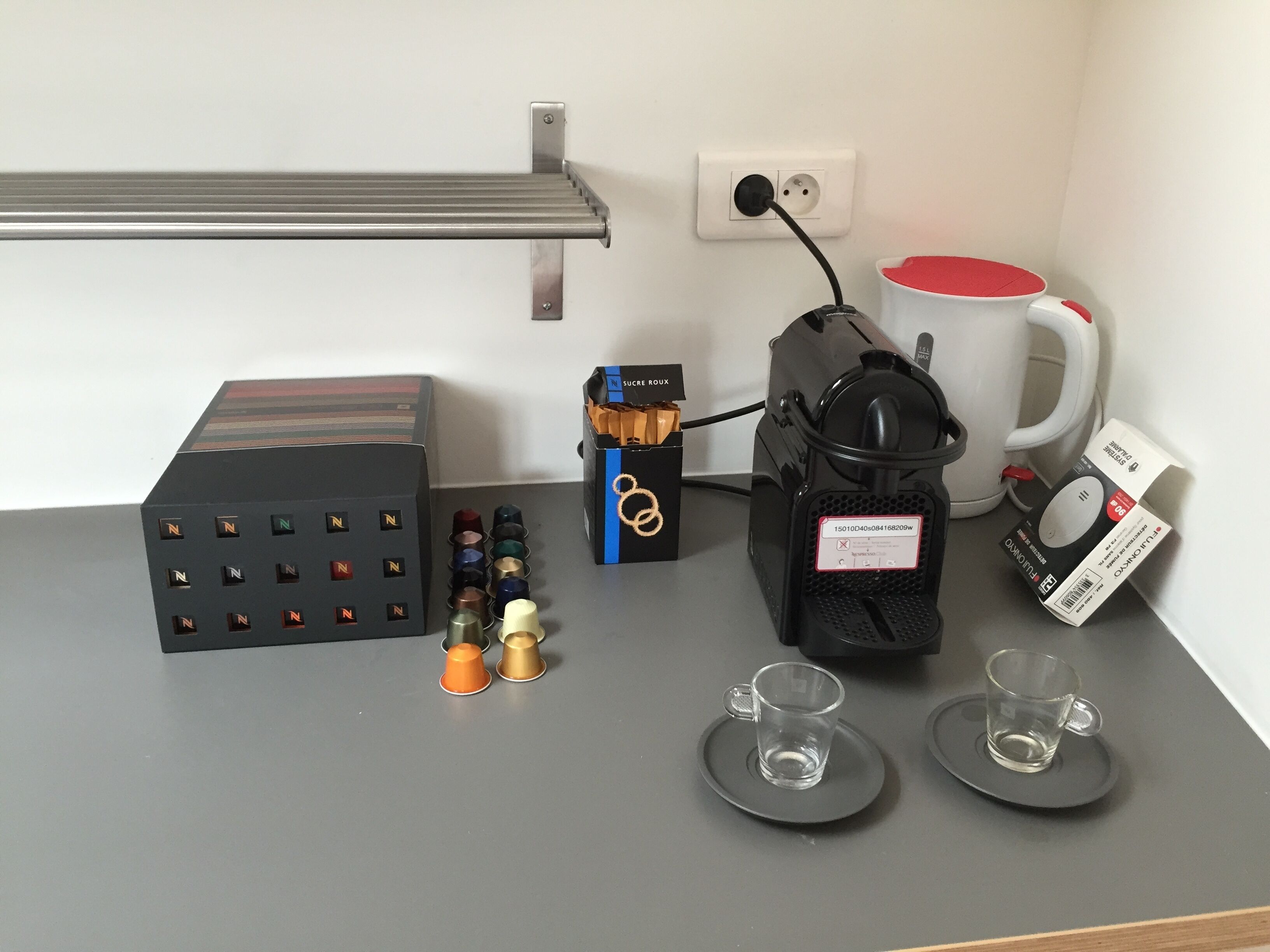 A coffee machine, a box of coffee pods, two cups, and a mug on a table.