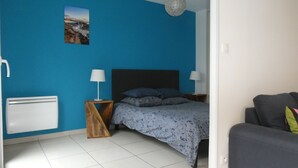 A bedroom with a bed, two bedside tables with lamps, a radiator, a picture on the wall, and a grey sofa in the corner. - Proche Plage & remparts, T1bis, terrace, Wifi, parking space, bed made (Saint-Malo)
