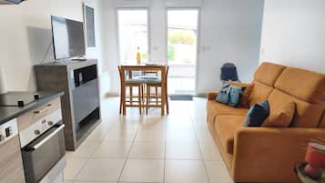 A modern kitchen with a dining area, a sofa, and a television.
