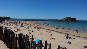 A crowded beach with people sunbathing and swimming, a historic building, and a clear blue sky. - Proche Plage & remparts, T1bis, terrace, Wifi, parking space, bed made (Saint-Malo)