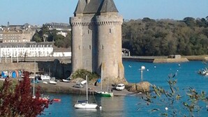 A castle with a tower by a body of water, surrounded by greenery and buildings. - Proche Plage & remparts, T1bis, terrace, Wifi, parking space, bed made (Saint-Malo)