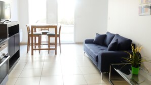 A modern living room with a dark blue sofa, a dining table with chairs, a TV, and a small green plant on a glass table. - Proche Plage & remparts, T1bis, terrace, Wifi, parking space, bed made (Saint-Malo)