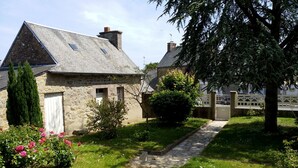 A stone house with a sloped roof, a white door, and a garden with pink flowers and a pathway leading to a gate. - Large home park, in a small Breton village 4 km from the sea  (Kerfot)