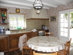 A kitchen with wooden cabinets, a dining table with a floral tablecloth, a sink, and a clock on the wall.