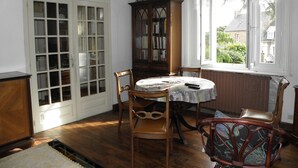 A room with a round table, wooden chairs, a bookcase, and a window with a view of greenery. - Large home park, in a small Breton village 4 km from the sea  (Kerfot)