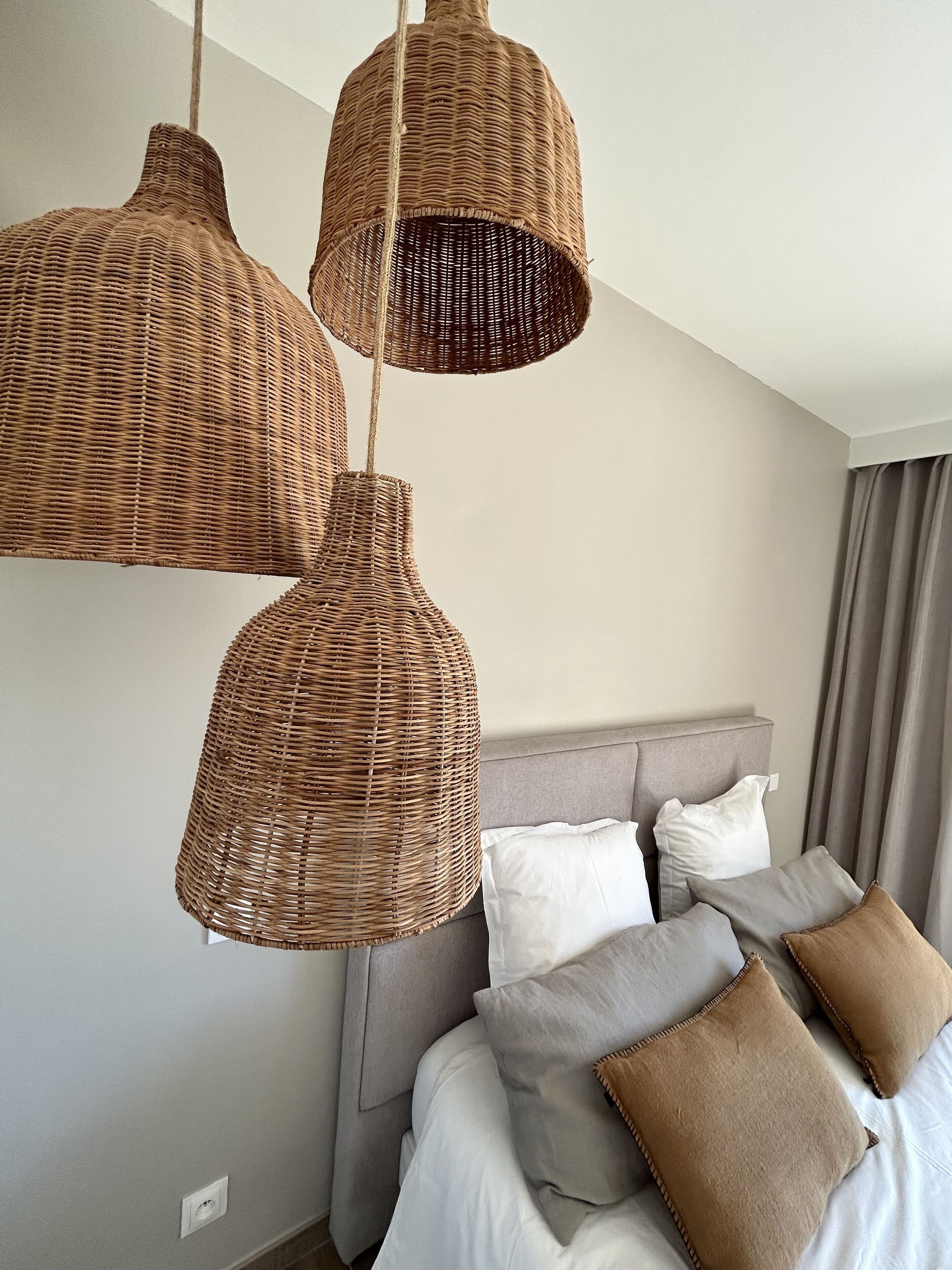 A bedroom with a bed, grey headboard, and three wicker pendant lights.