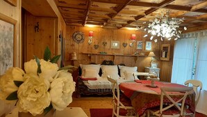 A cozy room with wooden walls, a dining table with chairs, a vase of flowers, and a chandelier. - A cottage in a garden in Rougegoutte (Rougegoutte)