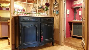 A wooden cabinet with decorative handles and a glass top, surrounded by shelves with various items. - A cottage in a garden in Rougegoutte (Rougegoutte)