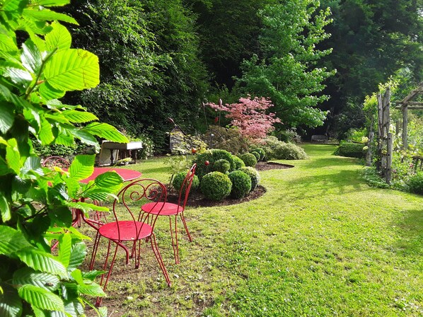 A garden with a red metal table and chairs, surrounded by well-maintained grass and various plants.