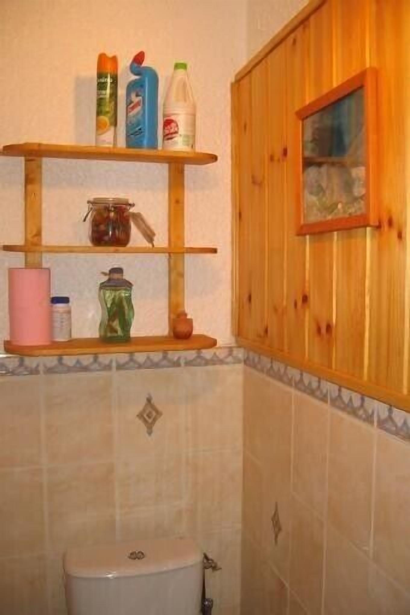 Une salle de bain avec une étagère en bois où sont rangés les articles de toilette, des toilettes et une fenêtre donnant sur l’extérieur.