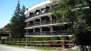 A multi-story building with balconies, surrounded by greenery and a wooden fence.