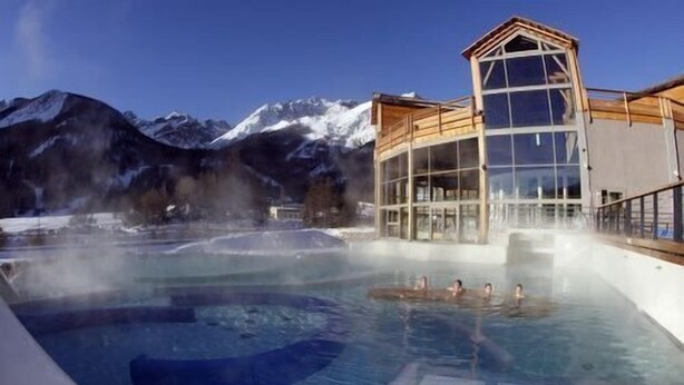 A hot spring pool with a wooden building and mountains in the background.