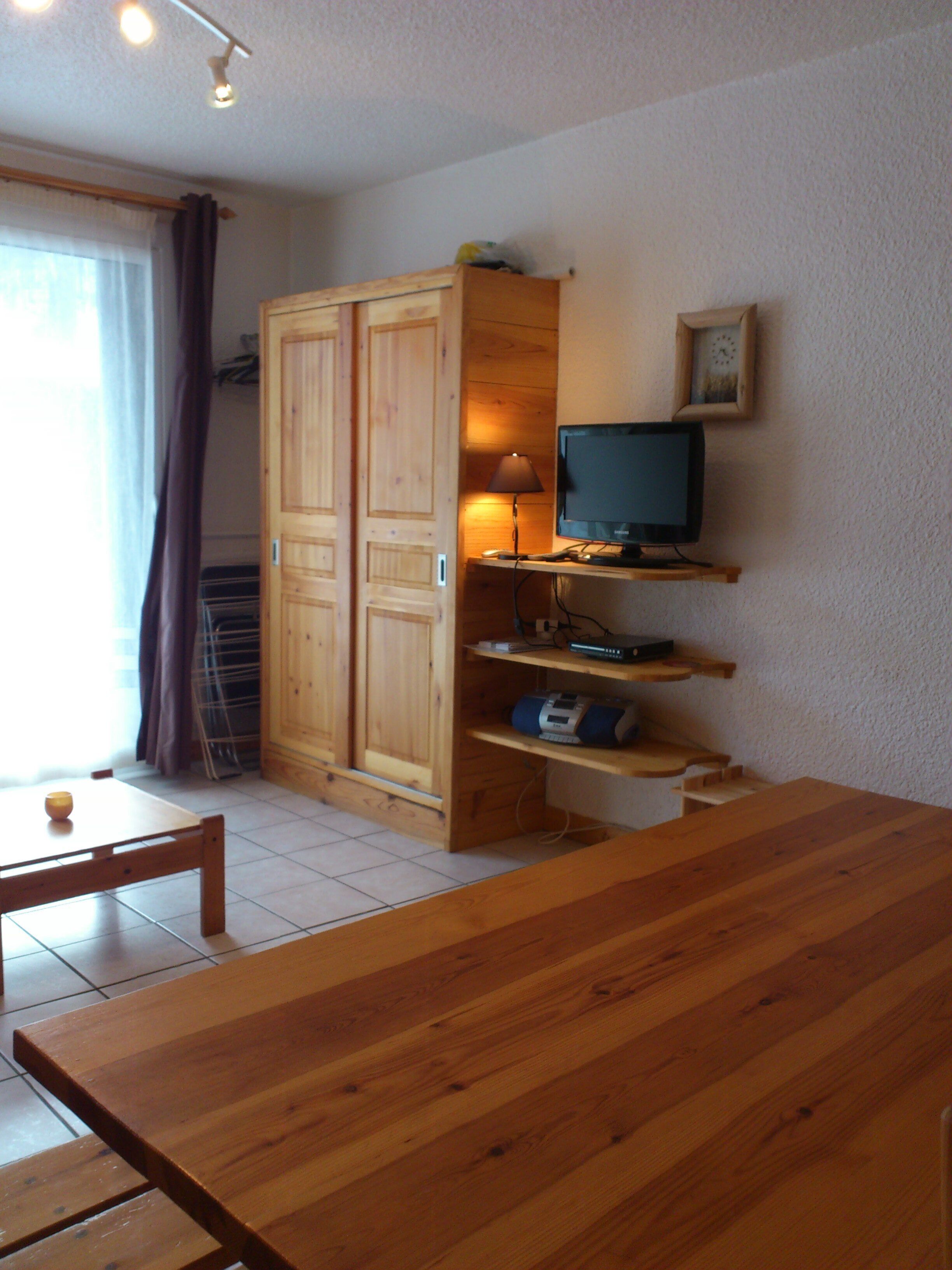 Een kamer met een houten tafel, een televisie op een plank en een kledingkast.