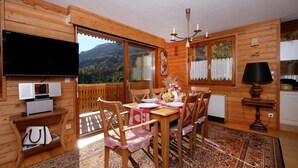 Una cabaña de madera con comedor que incluye una mesa dispuesta para cuatro personas, un televisor y vistas a las montañas.