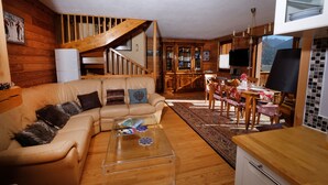 Una sala de estar acogedora con una escalera de madera, comedor y cocina con armarios de madera y vistas a las montañas.