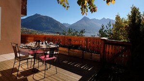 Una terraza de madera con una mesa y sillas, con vistas a un paisaje montañoso.