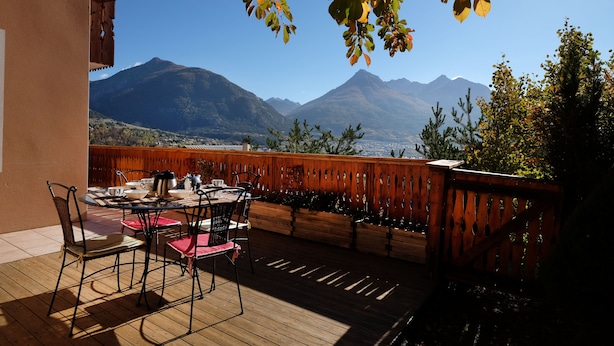 Una terraza de madera con una mesa y sillas, con vistas a un paisaje montañoso.