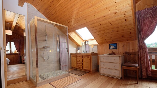 Interior de una cabaña de madera con ducha de vidrio, armarios de madera, una pequeña zona de estar y un tragaluz.