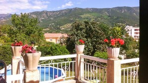 A balcony with a view of mountains, a swimming pool, and potted plants.