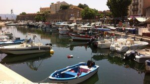 A marina with various boats docked, a stone wall, and buildings in the background.